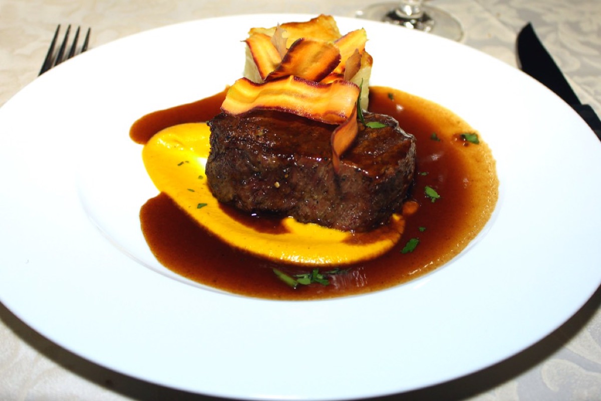 A grilled steak fillet in red wine jus with roasted parsnip crisps and squash puree on a white plate