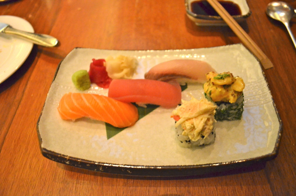 A rectangular plate with a selection of nigiri and sashimi including salmon, tuna and shrimp, with wasabi and pickled ginger
