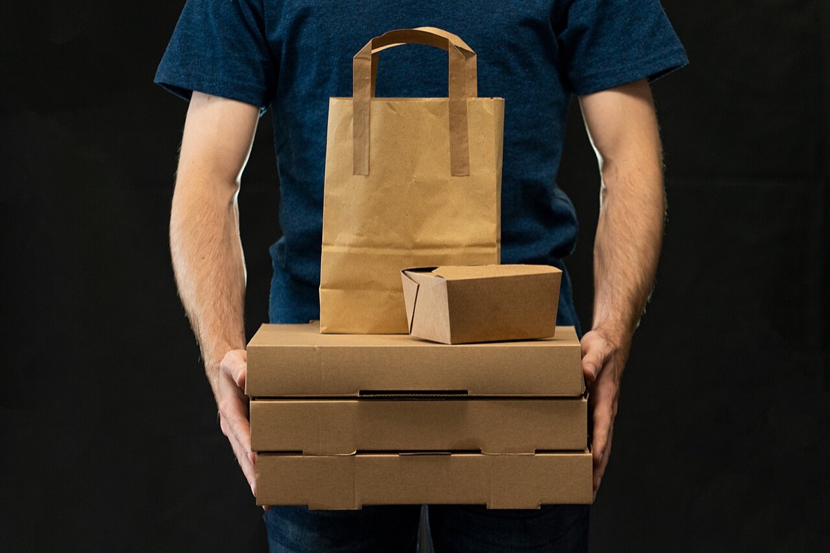 Person holding a stack of takeaway pizza boxes, a food container and a paper bag