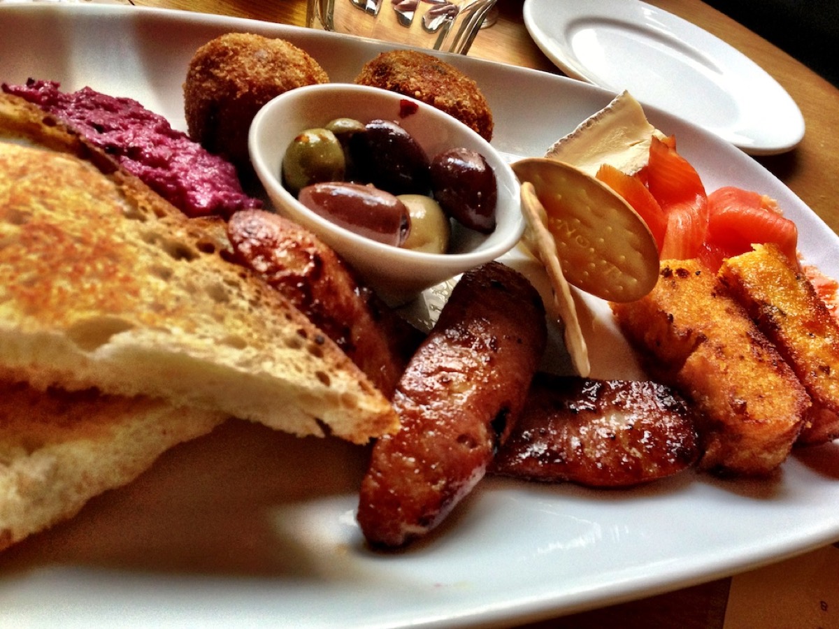 A tapas sampler plate with toasted bread, beetroot dip, chorizo, olives, salmon, brie and croquettes