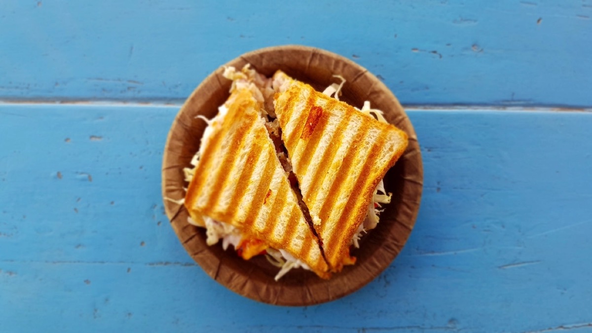 A grilled panini sandwich with char lines, cut in half, in a paper bowl on a blue painted surface