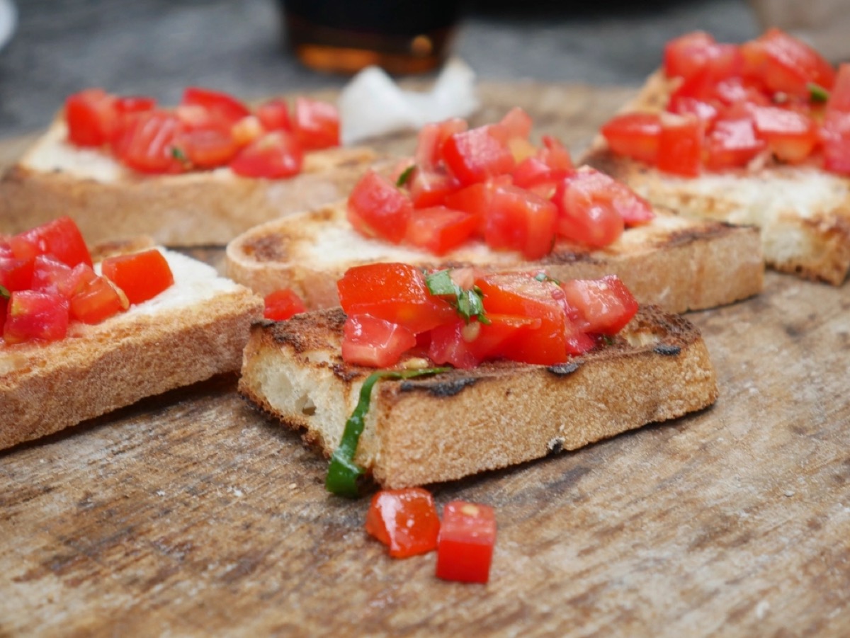 Slices of grilled sourdough topped with diced tomato and basil bruschetta on a wooden board