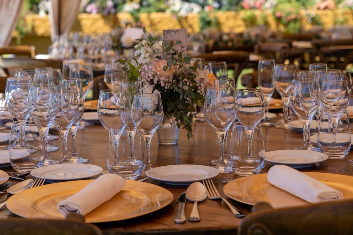 Wedding reception table set with wine glasses, gold chargers and a floral centrepiece